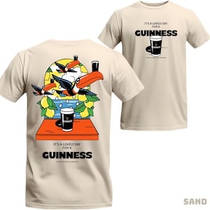 Peut inclure: T-shirt couleur sable avec un motif Guinness. L'avant affiche un verre de Guinness et le texte "IT'S A LOVELY DAY FOR A GUINNESS". Le dos pr&eacute;sente des toucans, des citrons et un verre de Guinness. Un t-shirt d&eacute;contract&eacute; et amusant.