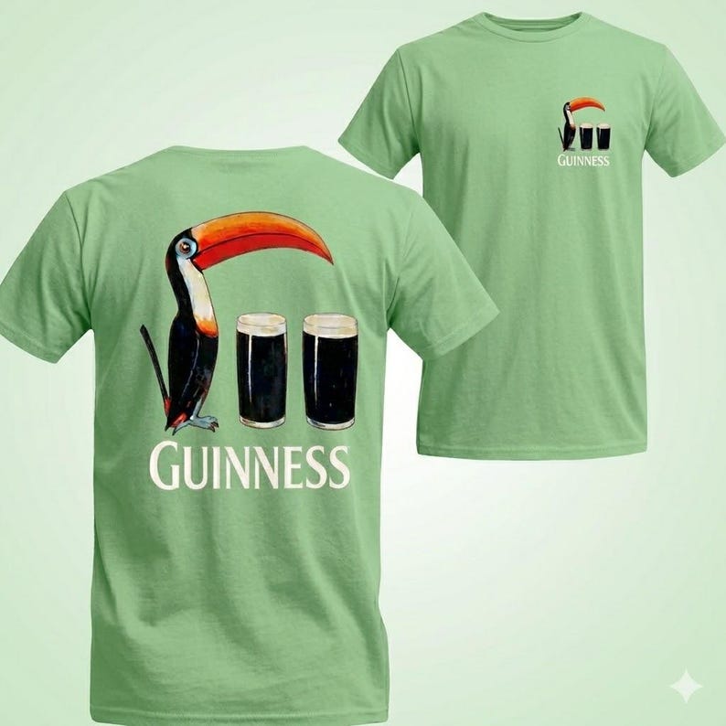 May include: Light green t-shirt featuring a toucan with a large orange beak, black and white feathers, and two pints of dark beer. The word "Guinness" is printed below the image. A smaller version of the design is on the front.