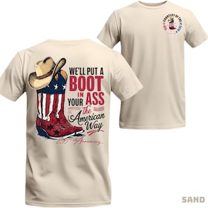 May include: A sand-coloured t-shirt with a graphic of a cowboy boot and hat, and the text "We'll put a boot in your ass the American way." The shirt also has a small circular graphic on the upper right chest with the text "Courtesy of the 76".