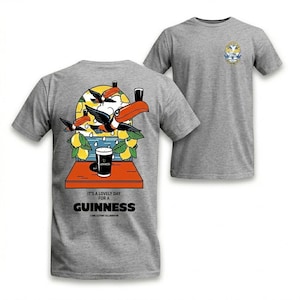 Puede incluir: Camiseta gris con un gr&aacute;fico colorido de tucanes, limones y una pinta de Guinness. El texto "It's a lovely day for a Guinness" est&aacute; impreso debajo. Un dise&ntilde;o m&aacute;s peque&ntilde;o est&aacute; en el pecho derecho.