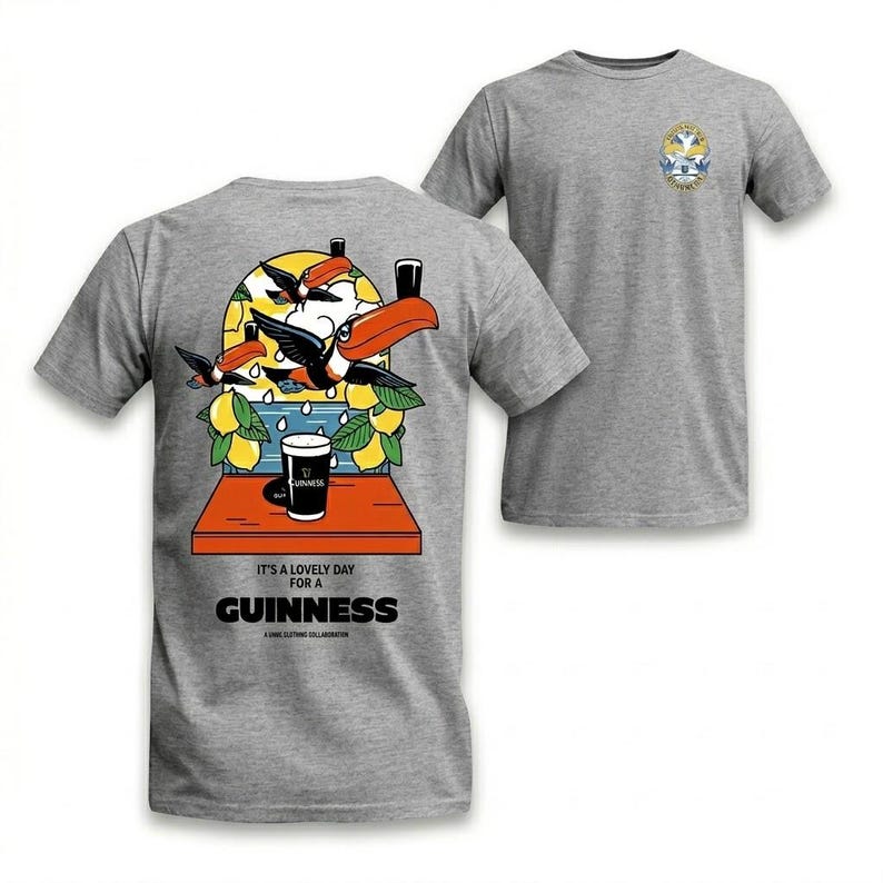 Puede incluir: Camiseta gris con un gr&aacute;fico colorido de tucanes, limones y una pinta de Guinness. El texto "It's a lovely day for a Guinness" est&aacute; impreso debajo. Un dise&ntilde;o m&aacute;s peque&ntilde;o est&aacute; en el pecho derecho.