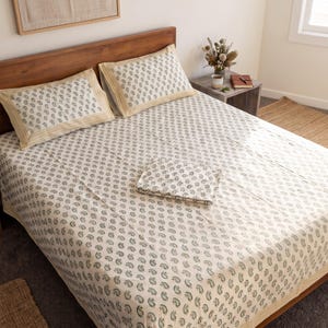 May include: A bed set featuring a cream-coloured bedspread and two matching pillowcases, all decorated with a repeating dark green paisley pattern. The pillowcases have a light yellow border with a subtle chevron design along the edges.