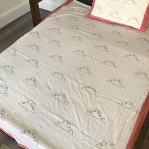 Pode incluir: Conjunto de roupa de cama branco com um padrão repetido de ilustrações de nuvens e estrelas em cinza, amarelo e azul. A almofada e as bordas do cobertor têm uma borda coral. A cama é de madeira escura.