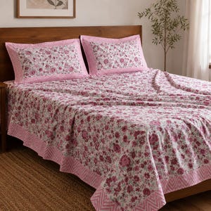 May include: A bed sheet set featuring a white base with a dense pink and red floral pattern. The set includes two rectangular pillowcases and a large flat sheet, all finished with a pink and white chevron-patterned border along the edges.