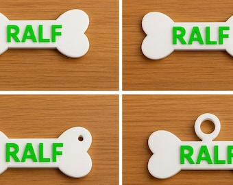 May include: Four white bone-shaped dog tags with the name "RALF" in green letters. Each tag has a different design: one plain, one with a hole, and two with a loop for attachment. The tags are on a wooden surface.