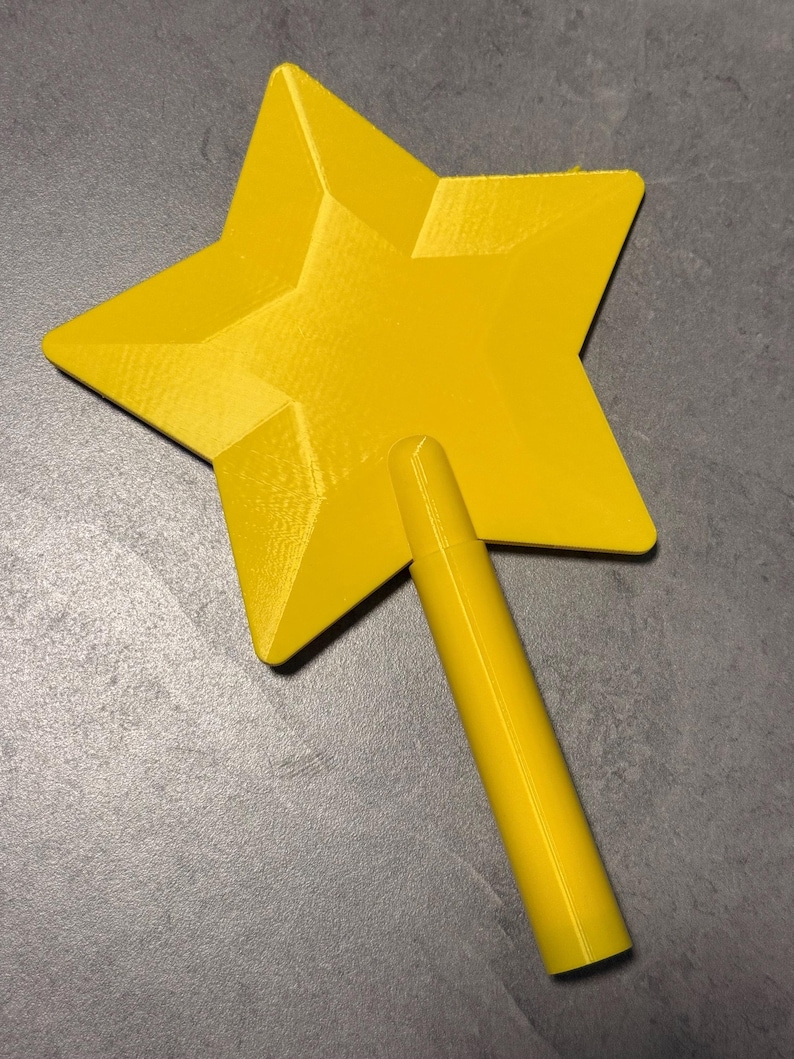 May include: A bright yellow star-shaped object with a smooth, faceted surface and a cylindrical handle attached to the bottom point. The item features a distinct geometric design with sharp angles and a uniform, solid colour finish throughout.