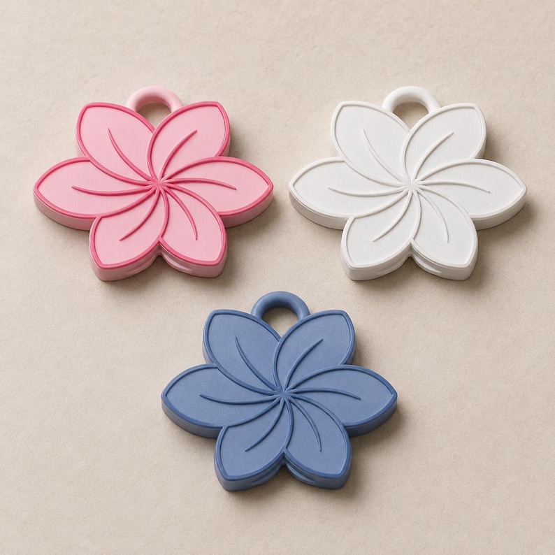 May include: Three flower-shaped silicone coasters in pink, white, and blue. Each coaster has a loop for hanging and a detailed floral design. The coasters are made of a soft, flexible material.