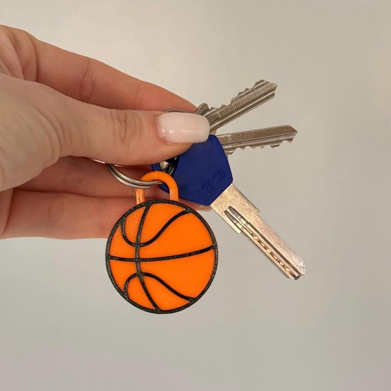 May include: A circular orange basketball keychain with black textured lines and a small orange loop at the top, attached to a silver metal keyring holding two standard silver keys and one key with a blue plastic head cover.