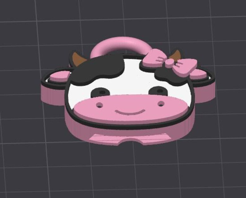 May include: A pink and black cow-shaped keychain with a bow on its head. The keychain has a white face with black spots, brown horns, and a pink nose. The keychain is made of a hard material.