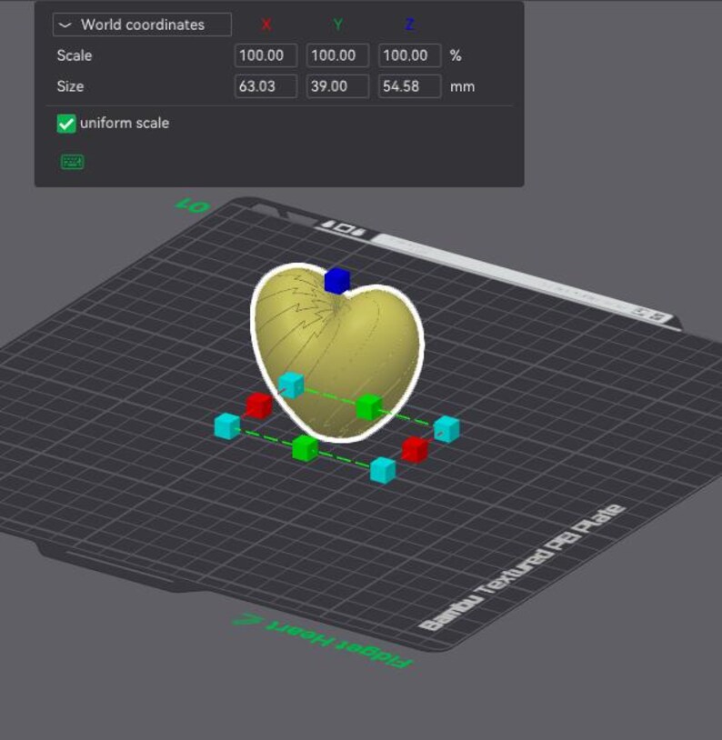May include: A 3D digital model of a heart-shaped object on a grid platform. The interface displays world coordinates with a scale of 100.00% and dimensions of 63.03 mm by 39.00 mm by 54.58 mm. The object is highlighted with a white outline and control cubes.