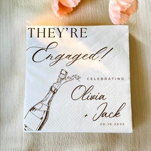 May include: White square paper napkin with the text "THEY'RE Engaged!" in elegant script. A champagne bottle illustration is featured, with the names Olivia and Jack, and the date 20.10.2025. Perfect for an engagement celebration.