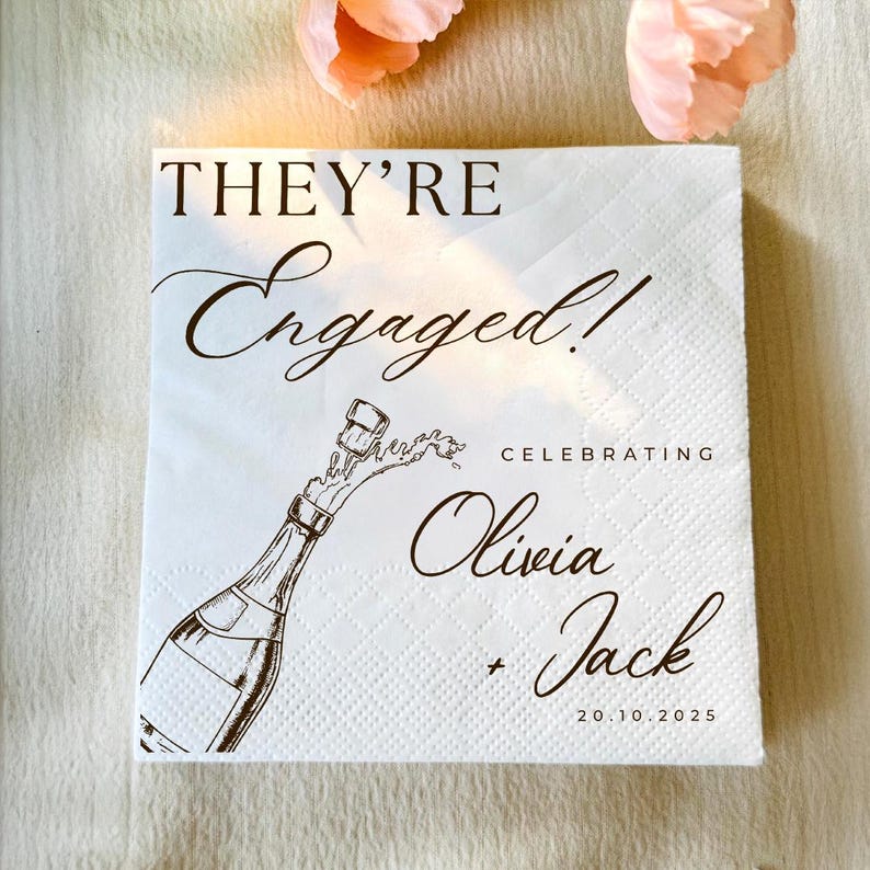 May include: White square paper napkin with the text "THEY'RE Engaged!" in elegant script. A champagne bottle illustration is featured, with the names Olivia and Jack, and the date 20.10.2025. Perfect for an engagement celebration.