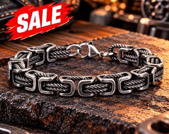 May include: A silver-toned metal chain bracelet featuring a repeating pattern of rectangular links connected by twisted wire segments. The bracelet includes a lobster claw clasp and is marked with a red graphic containing the word SALE.