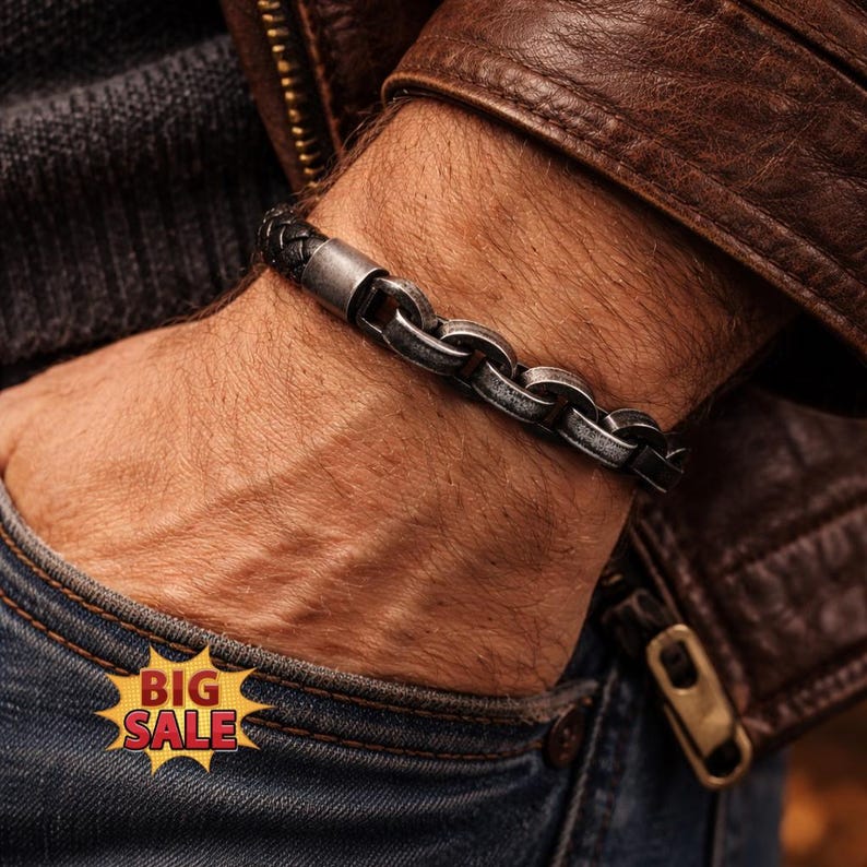 May include: A bracelet featuring a combination of black braided leather and a series of interconnected, weathered silver-toned metal links. The design includes a smooth, cylindrical metal clasp that secures the two distinct sections together.