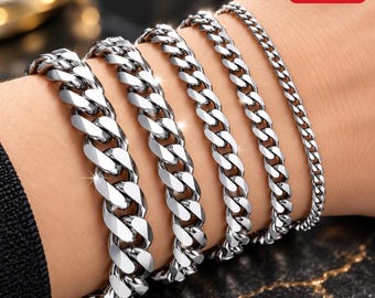 May include: A set of five silver-toned metal chain bracelets worn together. The bracelets feature interlocking curb links that vary in width, ranging from a thick, bold link style on the left to a thin, delicate chain on the far right.