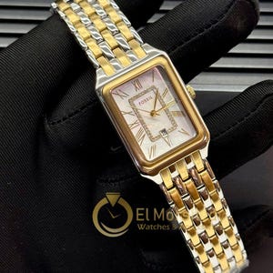 May include: A Fossil watch with a rectangular mother-of-pearl face, gold-tone bezel, and a two-tone gold and silver band. The watch face features Roman numerals and a small date display. The watch is displayed on a black surface.