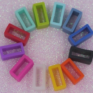 May include: A selection of brightly coloured silicone watch strap keepers. The keepers are in shades of red, pink, purple, orange, yellow, white, black, blue, green, and teal. They are arranged in a circle on a glittery pink surface.