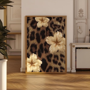 Puede incluir: Una obra de arte enmarcada con un fondo de estampado de leopardo y tres flores de hibisco crema tridimensionales. El marco es dorado. La obra de arte se exhibe en una habitación con pisos de madera y paredes blancas.