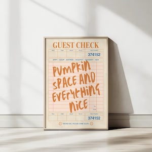 May include: A framed print resembling a vintage guest check. The text "GUEST CHECK" is at the top, with the words "Pumpkin Space and Everything Nice" in orange script. The print has a beige background and a wooden frame.