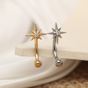 May include: Two star-shaped earrings, one gold-toned and one silver-toned, each with a small, clear gemstone at the center. The earrings have a curved design with a small ball at the bottom. The gold earring has a matching gold ball, while the silver earring has a silver ball.