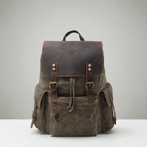 Pode incluir: Mochila resistente com aba e correias de couro marrom, combinada com um corpo de lona verde oliva. Possui vários bolsos, fivelas de latão e uma alça superior. Uma bolsa elegante e durável.