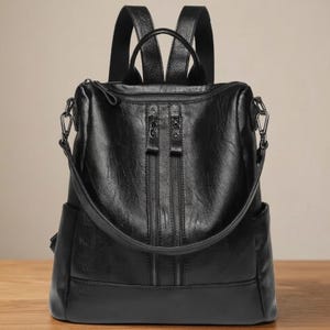 Puede incluir: Mochila de cuero negro con dos compartimentos verticales con cremallera en la parte delantera. La bolsa tiene un asa superior y correas ajustables para los hombros. También cuenta con una correa para el hombro desmontable y bolsillos laterales.