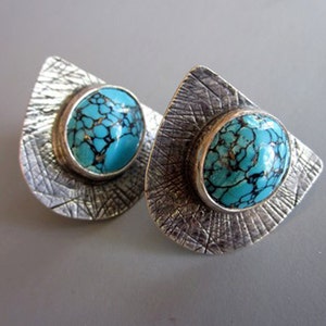 May include: A pair of silver earrings with turquoise stones set in textured silver. The stones have a blue and black marbled pattern.