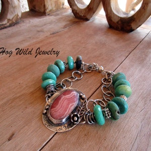 Könnte beinhalten: Ein silbernes Armband mit einem Anhänger aus rosa-weiß gestreiftem Stein und türkisfarbenen Perlen. Das Armband liegt auf einer Holzoberfläche. "Hog Wild Jewelry" steht in der oberen linken Ecke des Bildes.