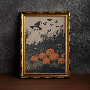 Puede incluir: Una impresi&oacute;n enmarcada con tem&aacute;tica de Halloween que presenta un fantasma con un sombrero de bruja, murci&eacute;lagos y calabazas. La obra de arte est&aacute; en un marco dorado y tiene un aspecto vintage ligeramente descolorido. Las calabazas tienen caras talladas.