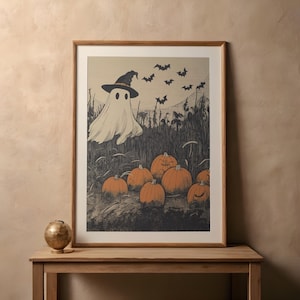 Puede incluir: Un cuadro enmarcado con una impresi&oacute;n art&iacute;stica de Halloween que presenta un fantasma con sombrero de bruja, rodeado de calabazas y murci&eacute;lagos. La obra de arte de estilo vintage utiliza una paleta de colores neutros, ideal para la decoraci&oacute;n de temporada.