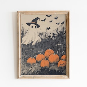 Puede incluir: Una impresi&oacute;n enmarcada con tem&aacute;tica de Halloween que presenta un fantasma con un sombrero de bruja, calabazas naranjas y murci&eacute;lagos. La obra de arte tiene un estilo vintage con una paleta de colores apagados en beige, negro y naranja.