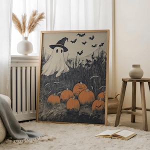 Puede incluir: Un estampado enmarcado de Halloween con un fantasma con sombrero de bruja, murci&eacute;lagos y calabazas naranjas. La obra de arte tiene un estilo vintage con una paleta de colores neutros, ideal para la decoraci&oacute;n de temporada. La impresi&oacute;n se muestra en una alfombra blanca.
