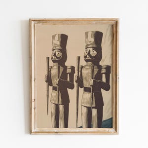 May include: Framed print featuring two toy soldier figures in a vintage style. The soldiers are depicted in a sepia tone with dark accents, holding staffs and wearing tall hats. The artwork is framed in a light-colored wooden frame.