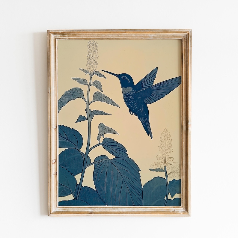 Peut inclure: Une impression encadr&eacute;e repr&eacute;sentant un colibri bleu en vol, approchant une plante &agrave; fleurs. L'&oelig;uvre d'art a une esth&eacute;tique vintage, avec un fond cr&egrave;me et un cadre en bois brun clair vieilli. Le colibri et la plante sont rendus en nuances de bleu.