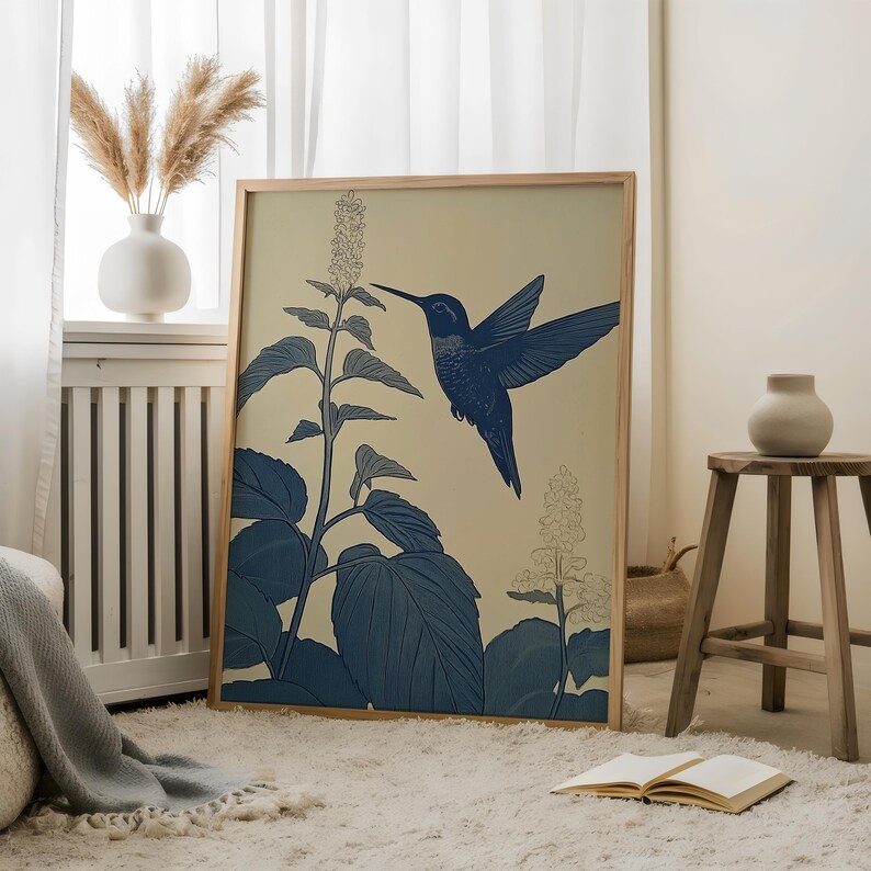 Peut inclure: Une affiche encadr&eacute;e repr&eacute;sentant un colibri bleu en vol, approchant une plante fleurie. L'&oelig;uvre d'art est pos&eacute;e sur un fond cr&egrave;me, avec la plante et l'oiseau rendus en nuances de bleu. Le cadre est en bois clair.