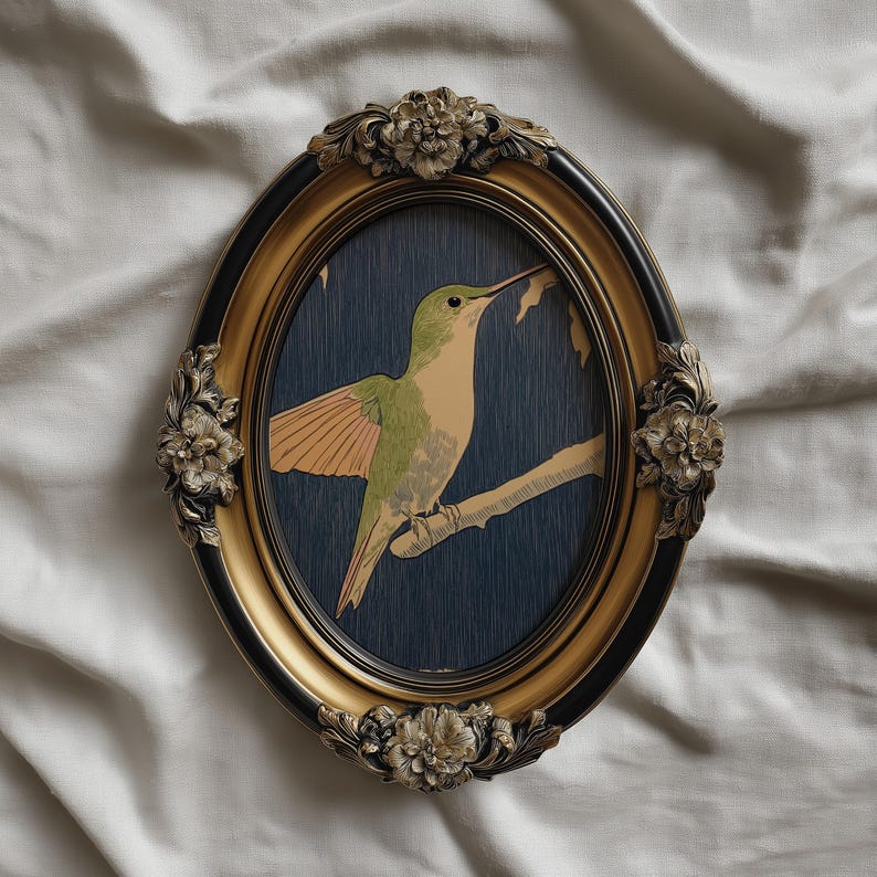 May include: Oval framed art print featuring a hummingbird perched on a branch. The bird has green and tan feathers with orange wings, set against a dark blue background. The frame is gold with black accents and floral embellishments.