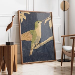 May include: A framed art print featuring a hummingbird perched on a branch. The artwork has a green and tan hummingbird against a dark blue background. The frame is a natural wood color. The print is leaning against a white wall.