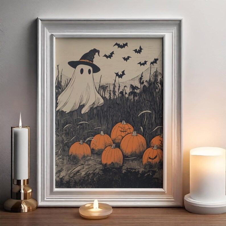 Puede incluir: Una impresi&oacute;n enmarcada con tem&aacute;tica de Halloween que presenta un fantasma con sombrero de bruja, murci&eacute;lagos y calabazas naranjas. La obra de arte de estilo vintage est&aacute; enmarcada en un marco blanco, ideal para la decoraci&oacute;n de temporada.