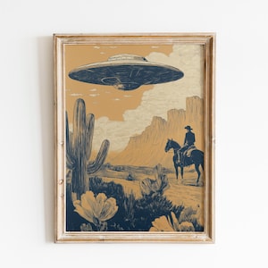 Könnte beinhalten: Gerahmter Kunstdruck mit einer Wüstenlandschaft, einem Cowboy auf einem Pferd und einem UFO darüber. Das Kunstwerk verwendet eine Farbpalette aus Beige, Blau und Creme. Ein großer Kaktus und Wüstenblumen befinden sich im Vordergrund.