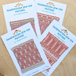 May include: Four cards with handwoven sew-on patches for visible mending. The patches feature red and cream geometric patterns. Each card has the text "HANDWOVEN SEW-ON PATCHES for Visible Mending" in blue. The patches are rectangular and have a woven texture.