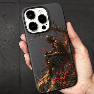 A person's hand holding a phone case with a painting of a knight in armor sitting on a rock, surrounded by flowers.