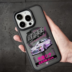 May include: A black and gray phone case featuring a purple sports car graphic. The case has the text "THE SPEED COMMUNITY" and Japanese text. The phone case is designed to fit a smartphone.