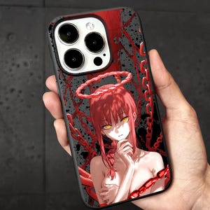 May include: Black phone case featuring a red-haired anime character with yellow eyes and a halo, surrounded by red chains. The case has a black border and a glossy finish, designed for a smartphone.