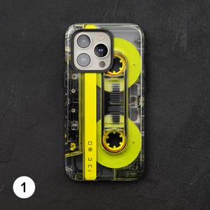 May include: Clear phone case with a retro cassette tape design. The case features a yellow and black cassette tape graphic, with a transparent border. The design includes Japanese text and a number 1 in white.