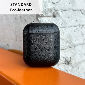 A black leather case is placed on an orange surface against a white brick wall.