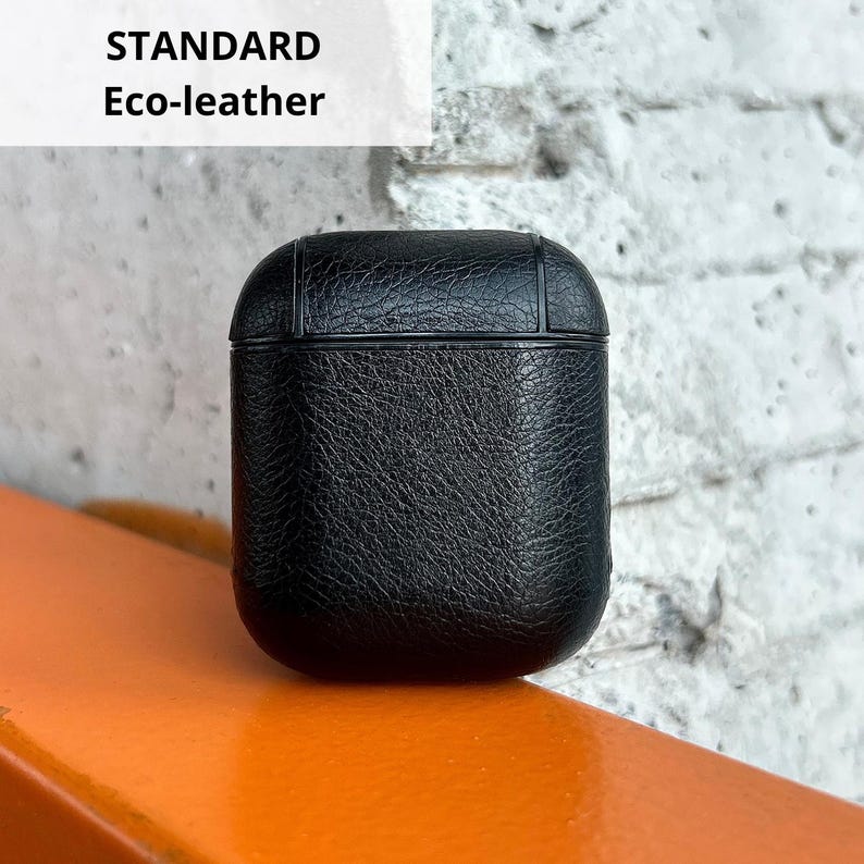 A black leather case is placed on an orange surface against a white brick wall.