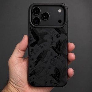 May include: A black smartphone case featuring a repeating pattern of dark grey crows in various flight and perched positions, interspersed with small floral vine elements. The case has a raised camera cutout section with three circular lenses.