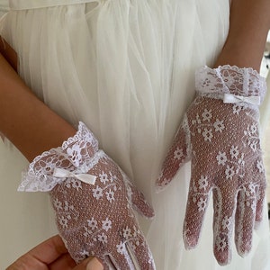 May include: A pair of white lace gloves with a small white bow on each wrist. The gloves are delicate and have a floral pattern.