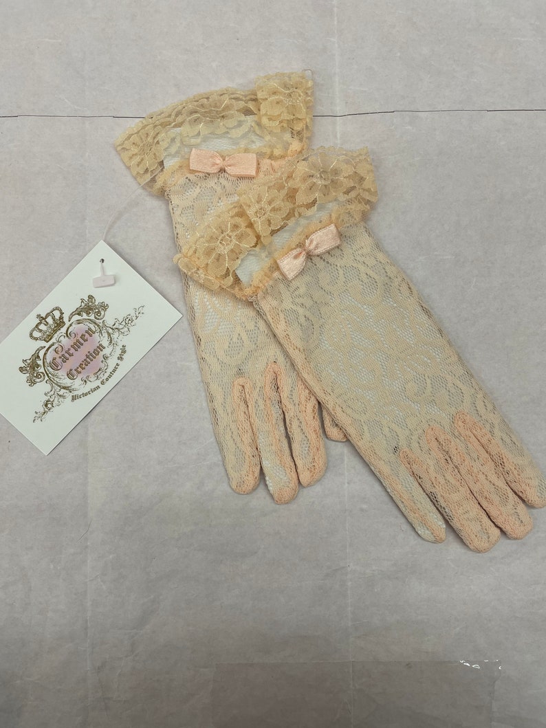 May include: A pair of ivory lace gloves with delicate pink bows. The gloves have a scalloped lace trim at the top and are made of a fine, sheer fabric.