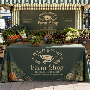 May include: A green market stall with a striped canopy and a table covered in a matching green cloth. The cloth and the backdrop sign feature the Durleighmarsh Farm Shop logo with a wheelbarrow graphic and the text The fruits of our labour.